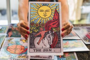 Zbliżenie na gigantyczną kartę tarota „Słońce” trzymaną przez wróżkę.