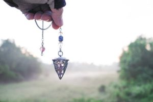 Przewidywanie przyszłości za pomocą kryształowego wahadła. Trzymanie i używanie kryształowego wahadła kwarcowego oraz korzystanie z niego, tło natury.