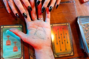 Wróżka zajmująca się czytaniem kart tarota, prezentująca ezoteryczny symbol misternie narysowany na dłoni, potęgujący mistyczną atmosferę.