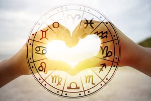 Dłonie kobiet i mężczyzn mają kształt serca, a przechodzące przez nie promienie słoneczne tworzą symbole astrologiczne
