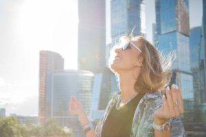 Stylowa, atrakcyjna kobieta siedzi na tle panoramy miasta i drapaczy chmur. Trzyma ręce w pozycji lotosu. Koncepcja wolności